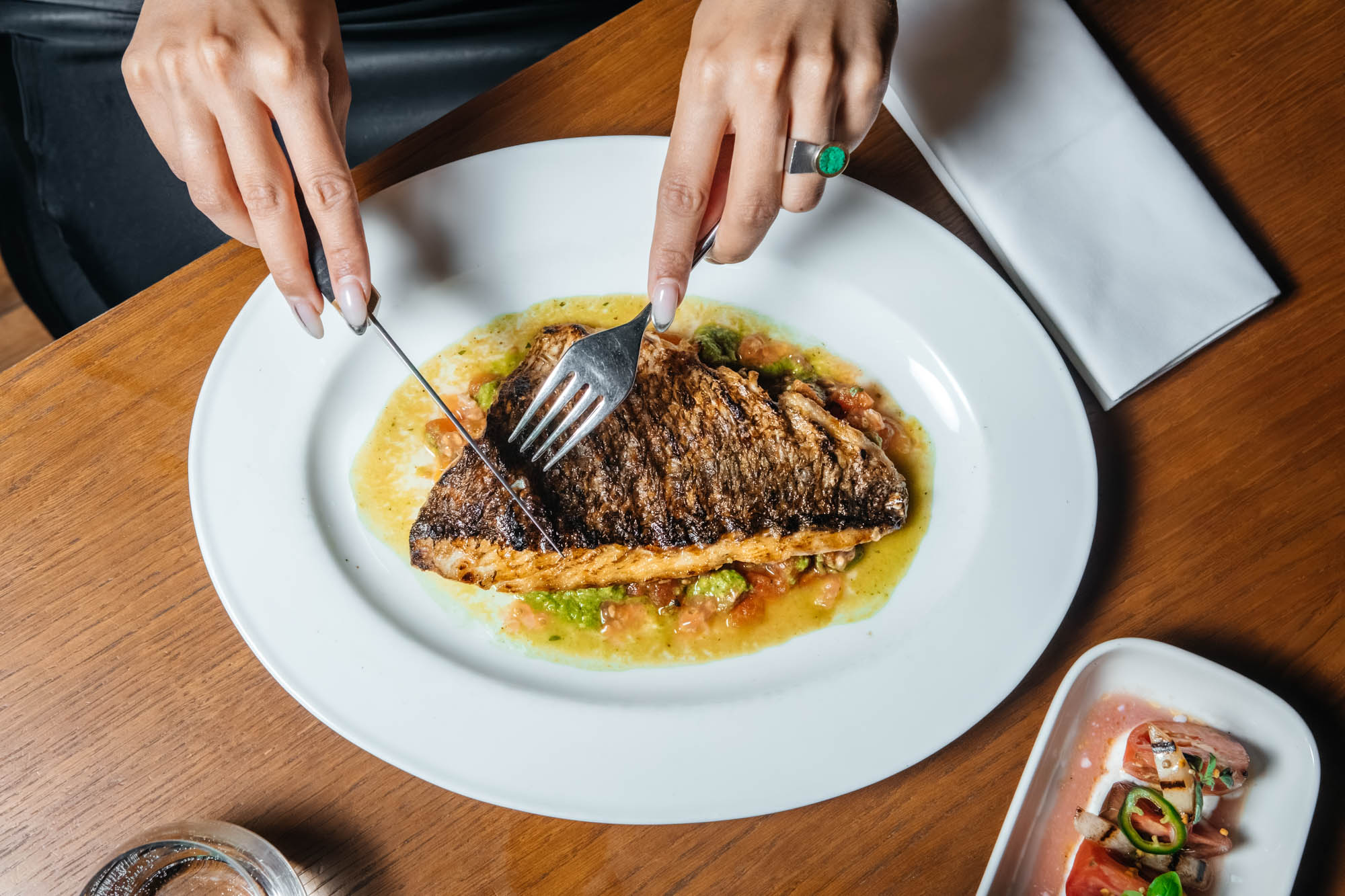 Manos cortando un filete de pescado con salsa en una mesa de MR PORTER Barcelona.