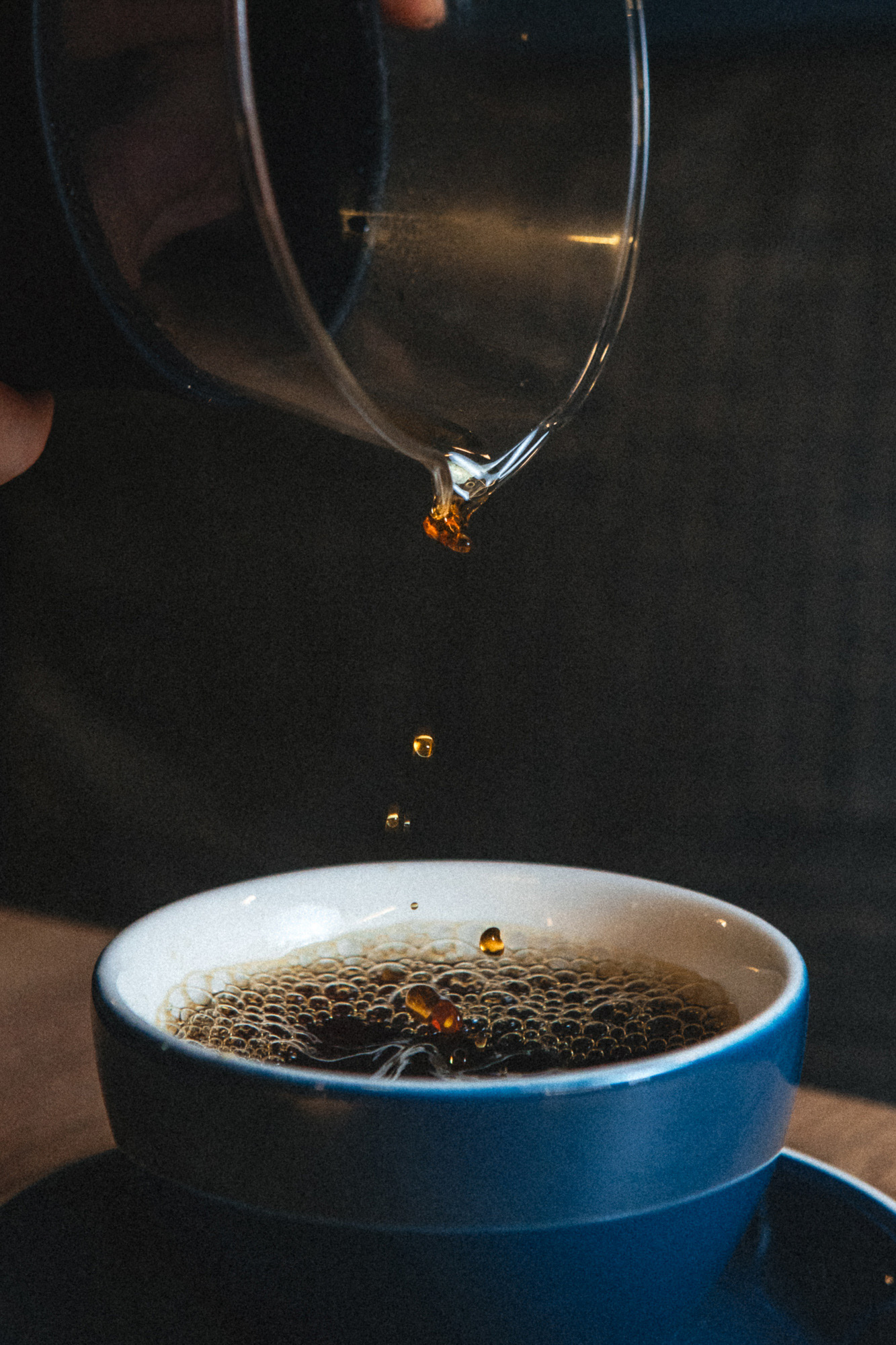 Café vertiéndose en una taza azul sobre fondo oscuro.