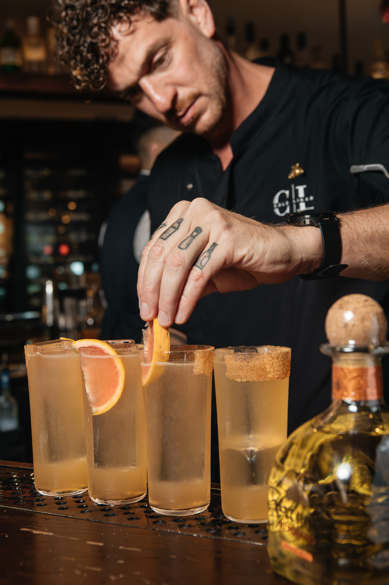 Barman preparando varios cócteles en una barra de madera.