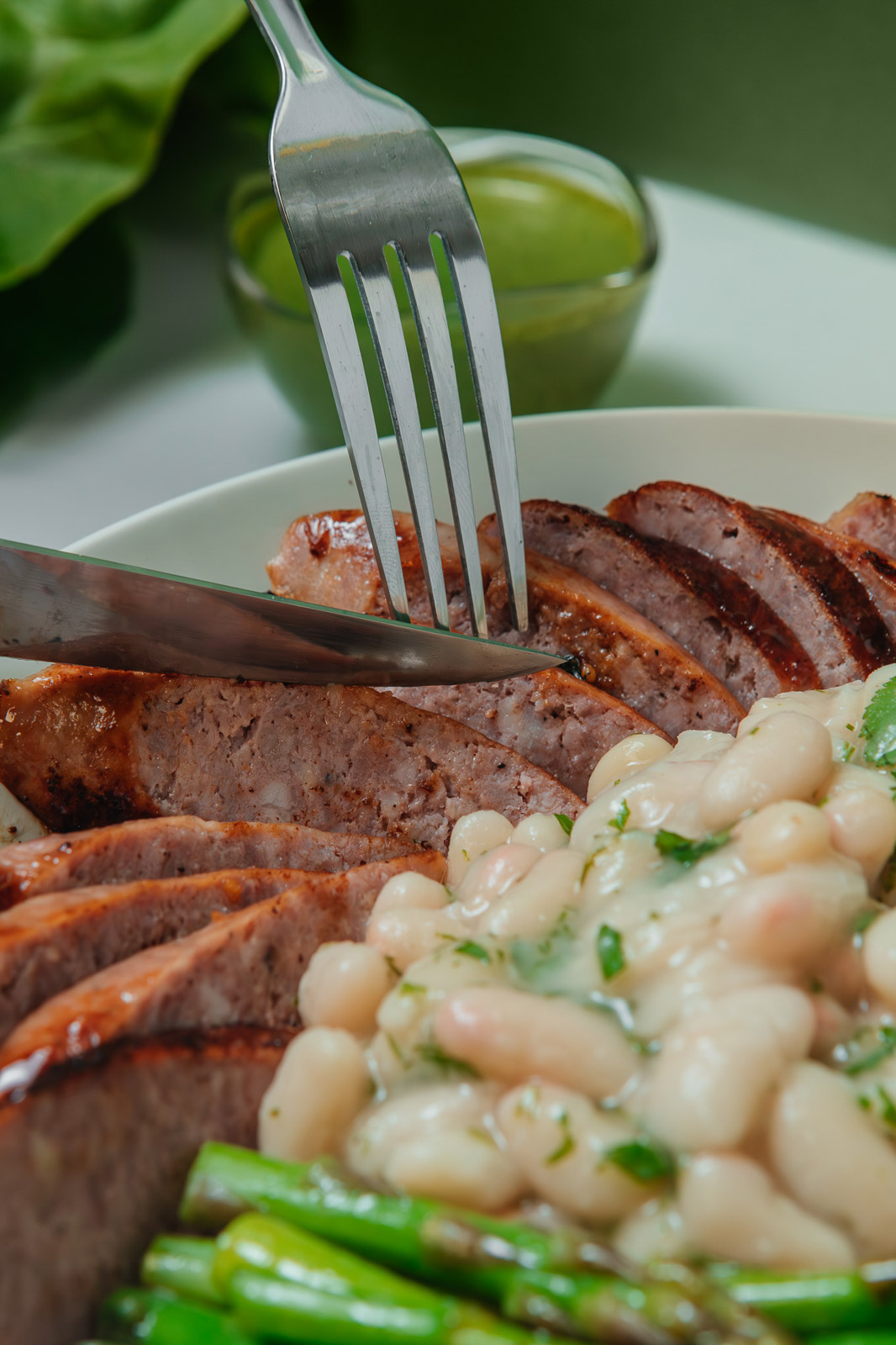 Tenedor sobre unas lonchas de carne acompañadas de judías blancas.