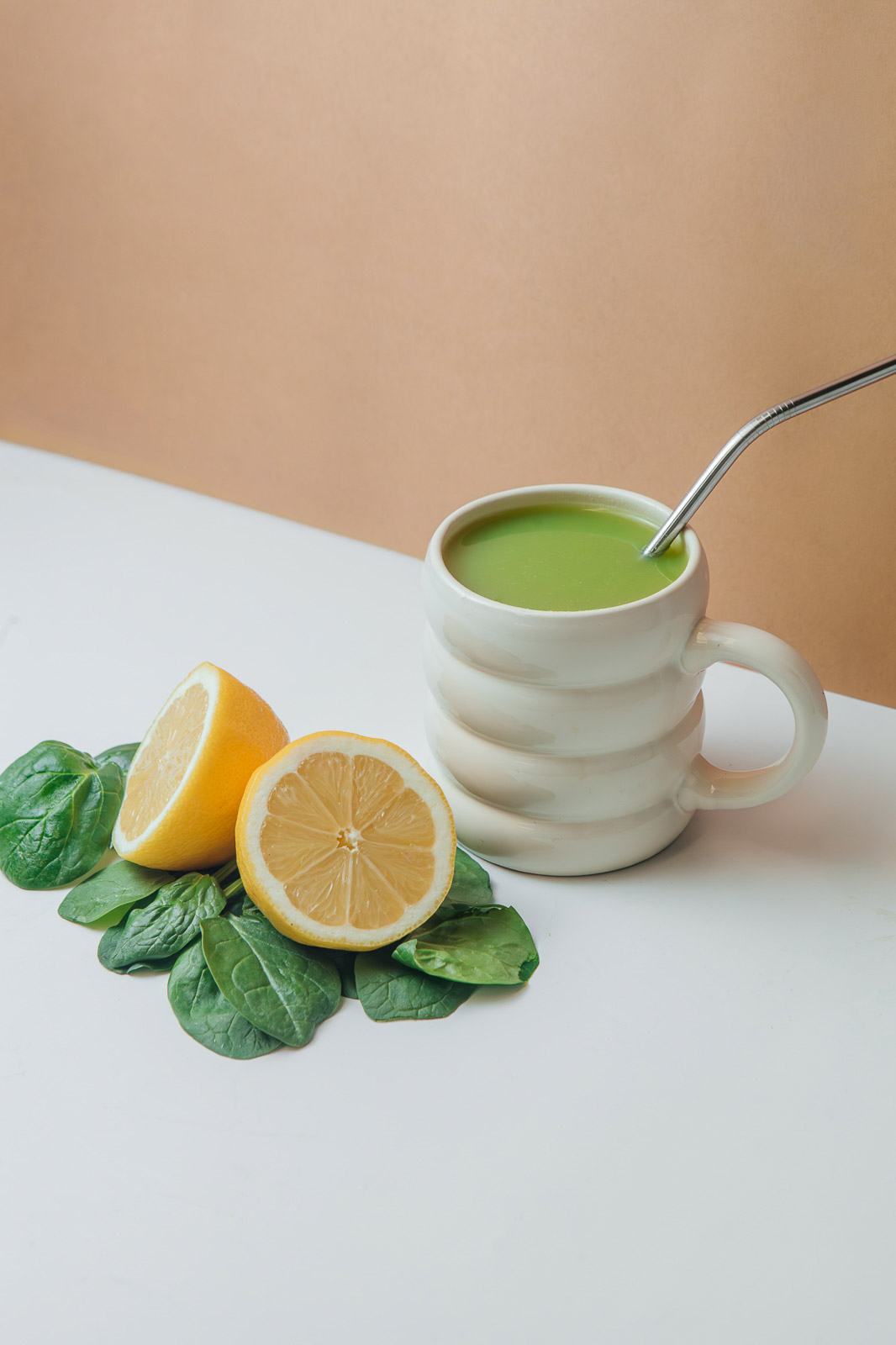 Taza con una preparación verde y una cuchara, junto a limón y hojas verdes.