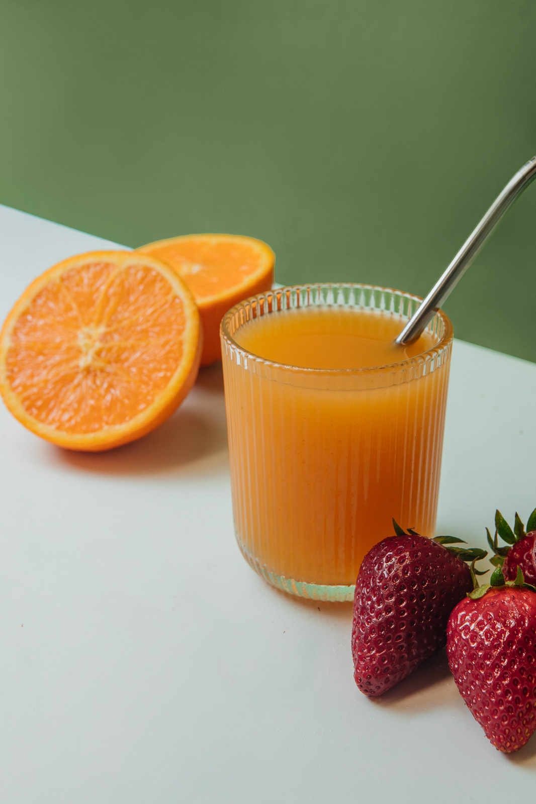 Zumo de naranja con pajita y una naranja cortada.