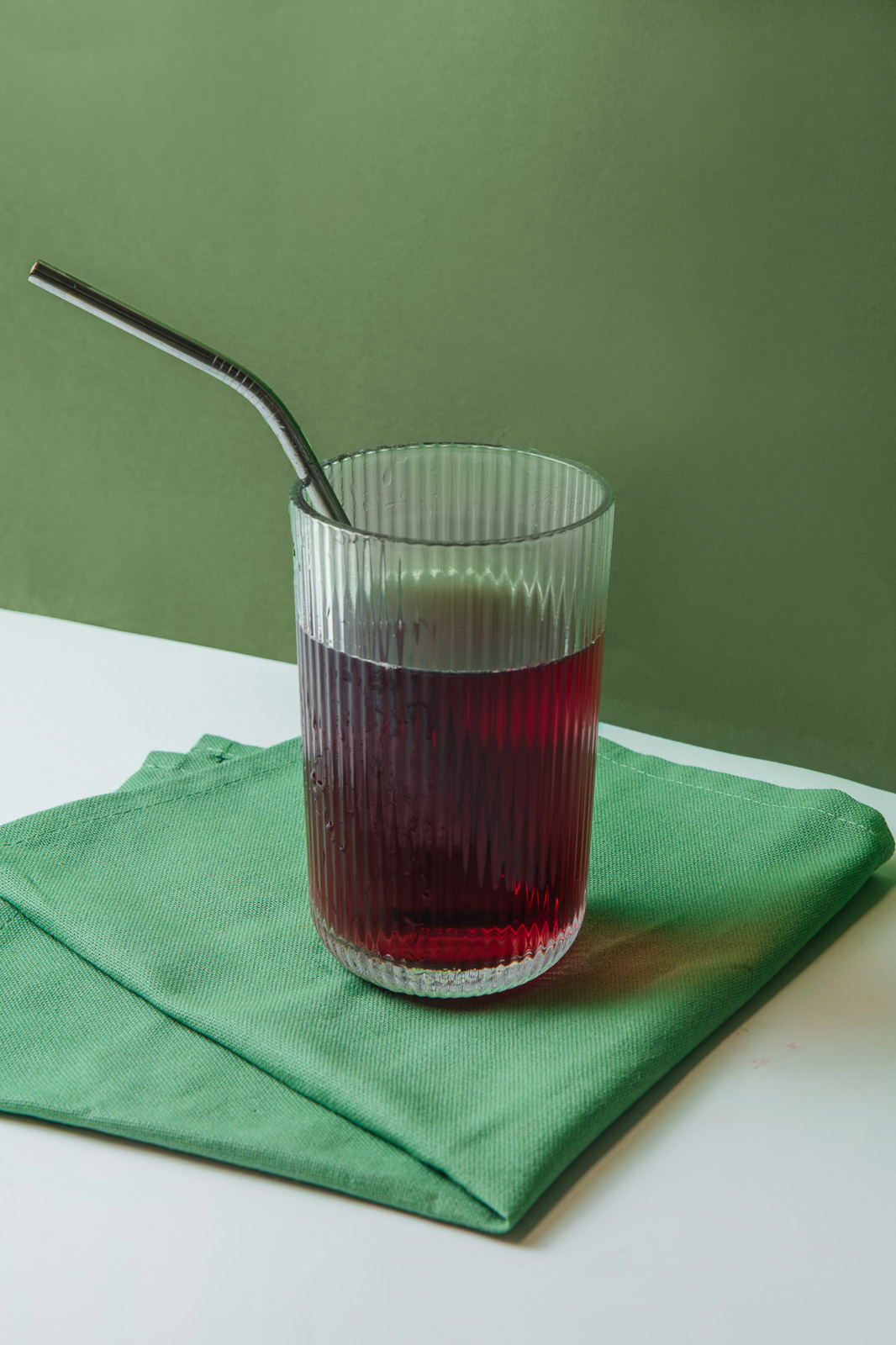 Bebida roja en un vaso con pajita sobre un fondo verde.