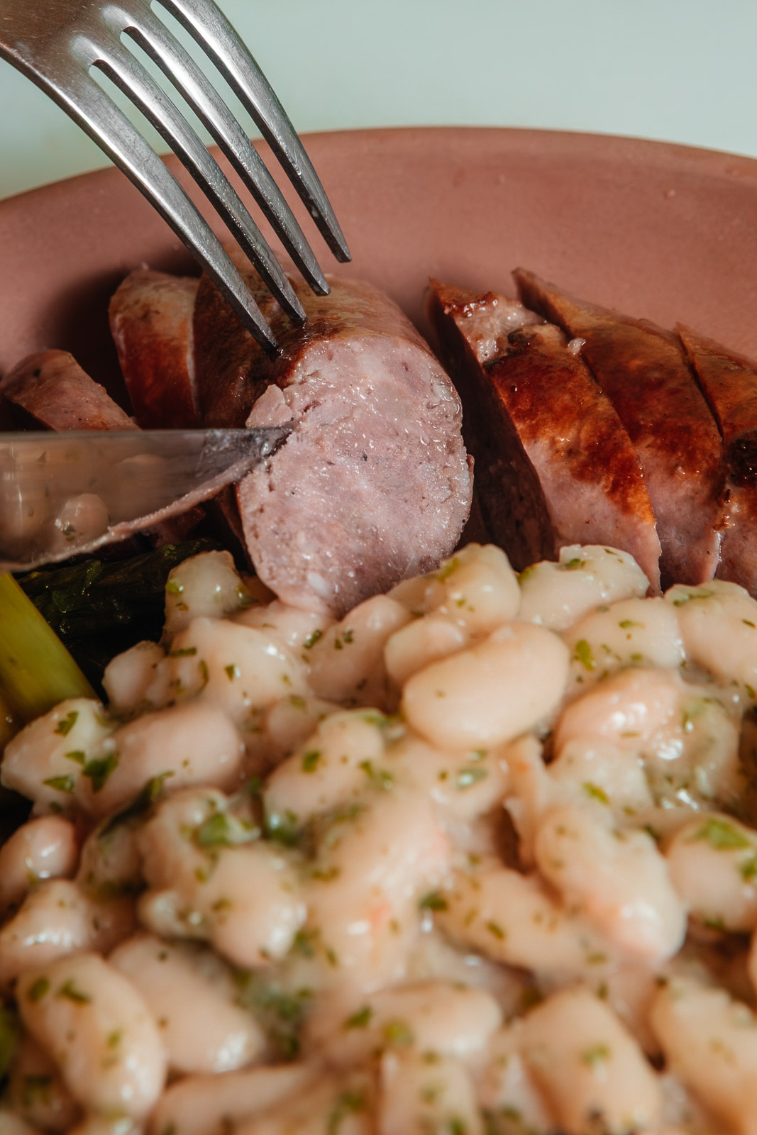 Detalle de carne cortada con cuchillo sobre un plato con judías blancas.