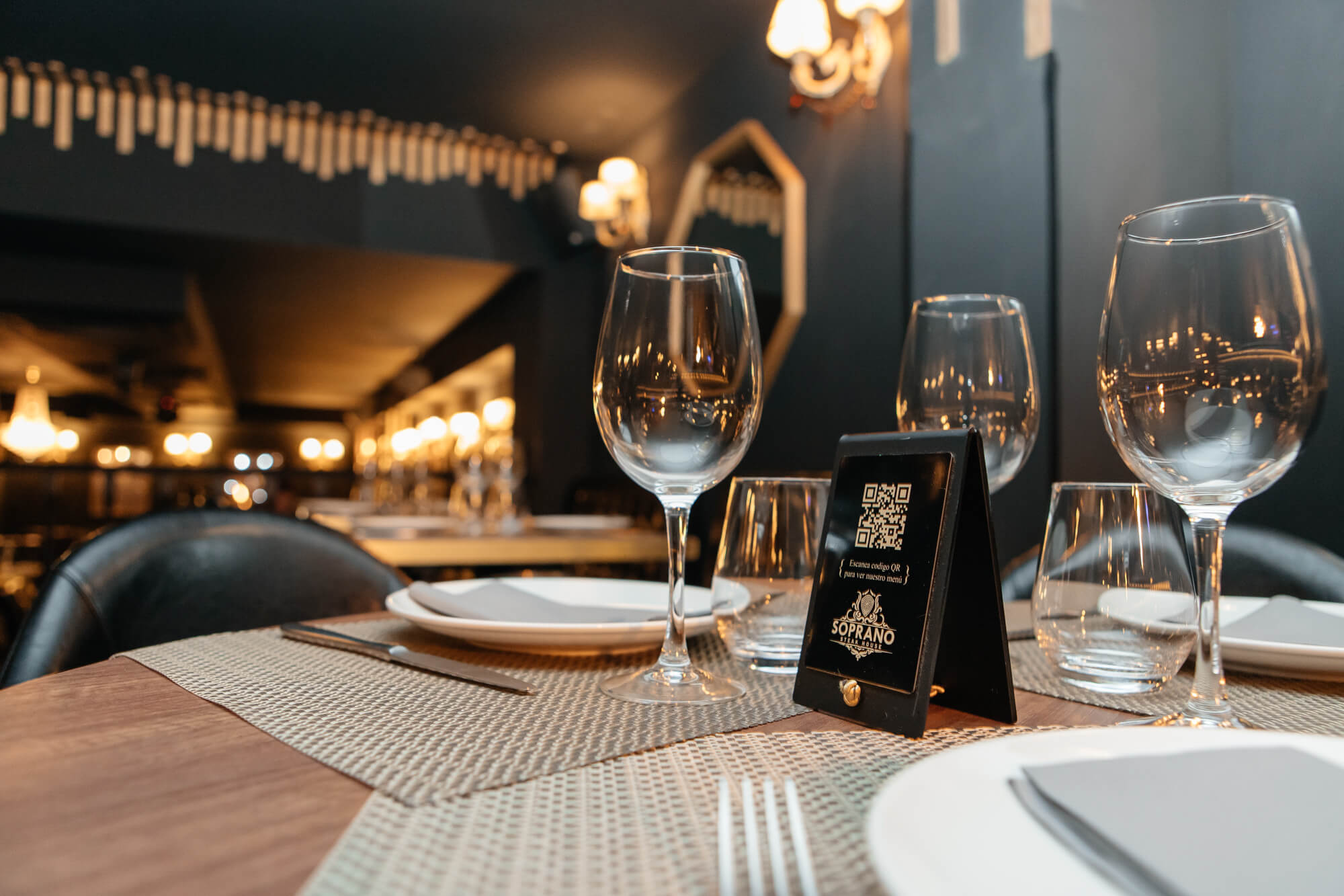 Mesa de restaurante preparada con platos, cubiertos y copas de vino.