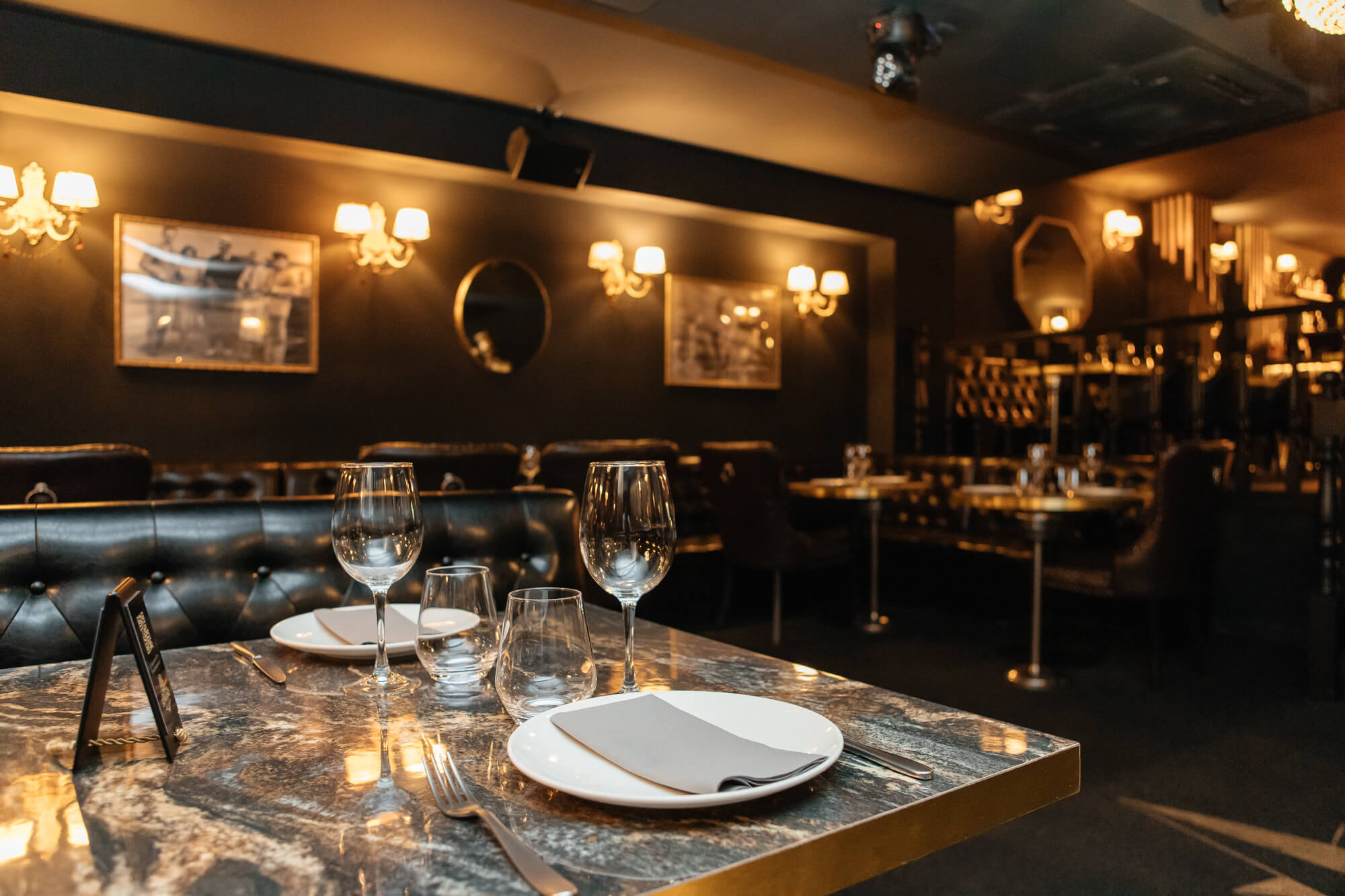 Interior de restaurante con mesas preparadas, copas de vino e iluminación cálida.