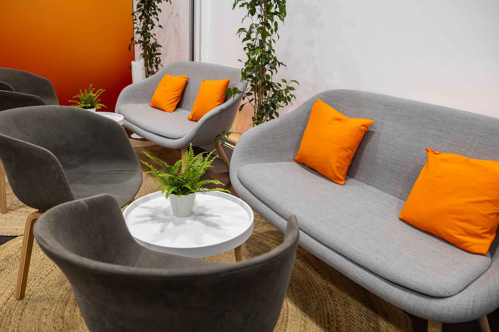 Zona lounge con sofás grises, cojines naranjas y mesas auxiliares en el espacio de GSK.