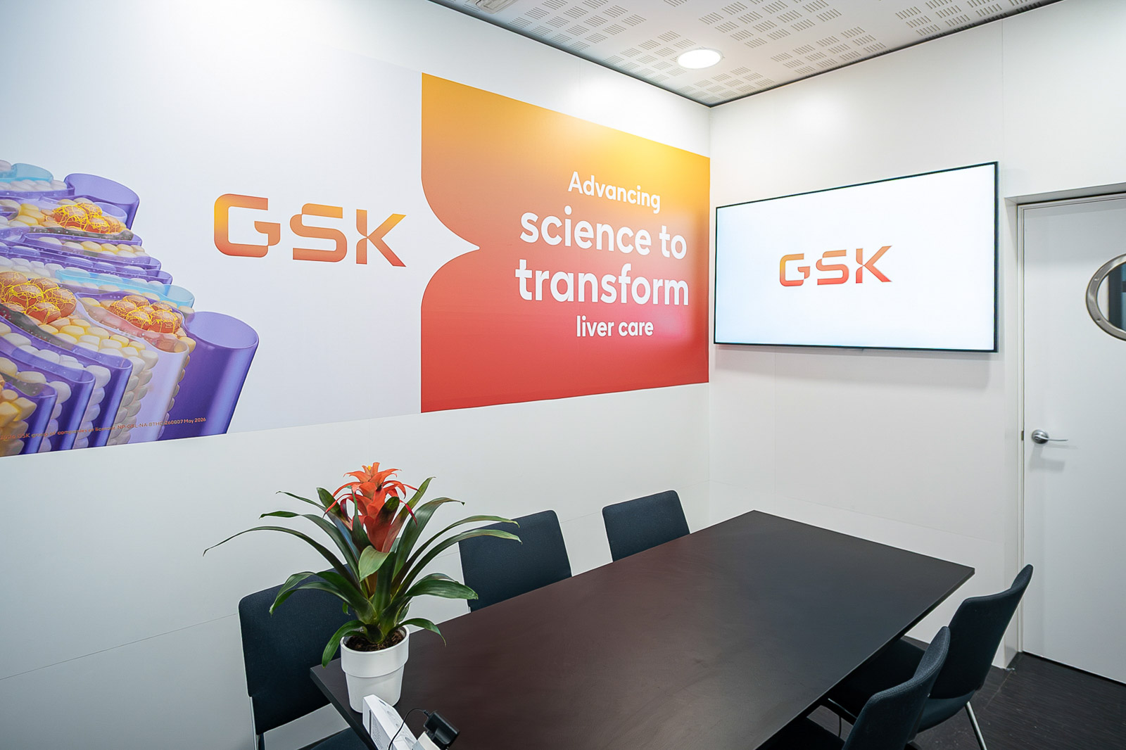 Sala de reuniones con mesa, sillas y elementos gráficos de GSK.
