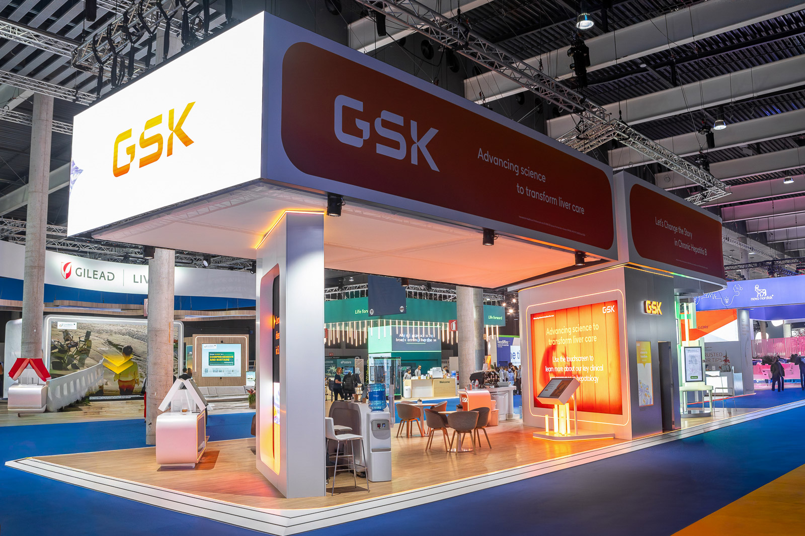 Vista exterior del stand de GSK en EASL, con estructura elevada e iluminación naranja.