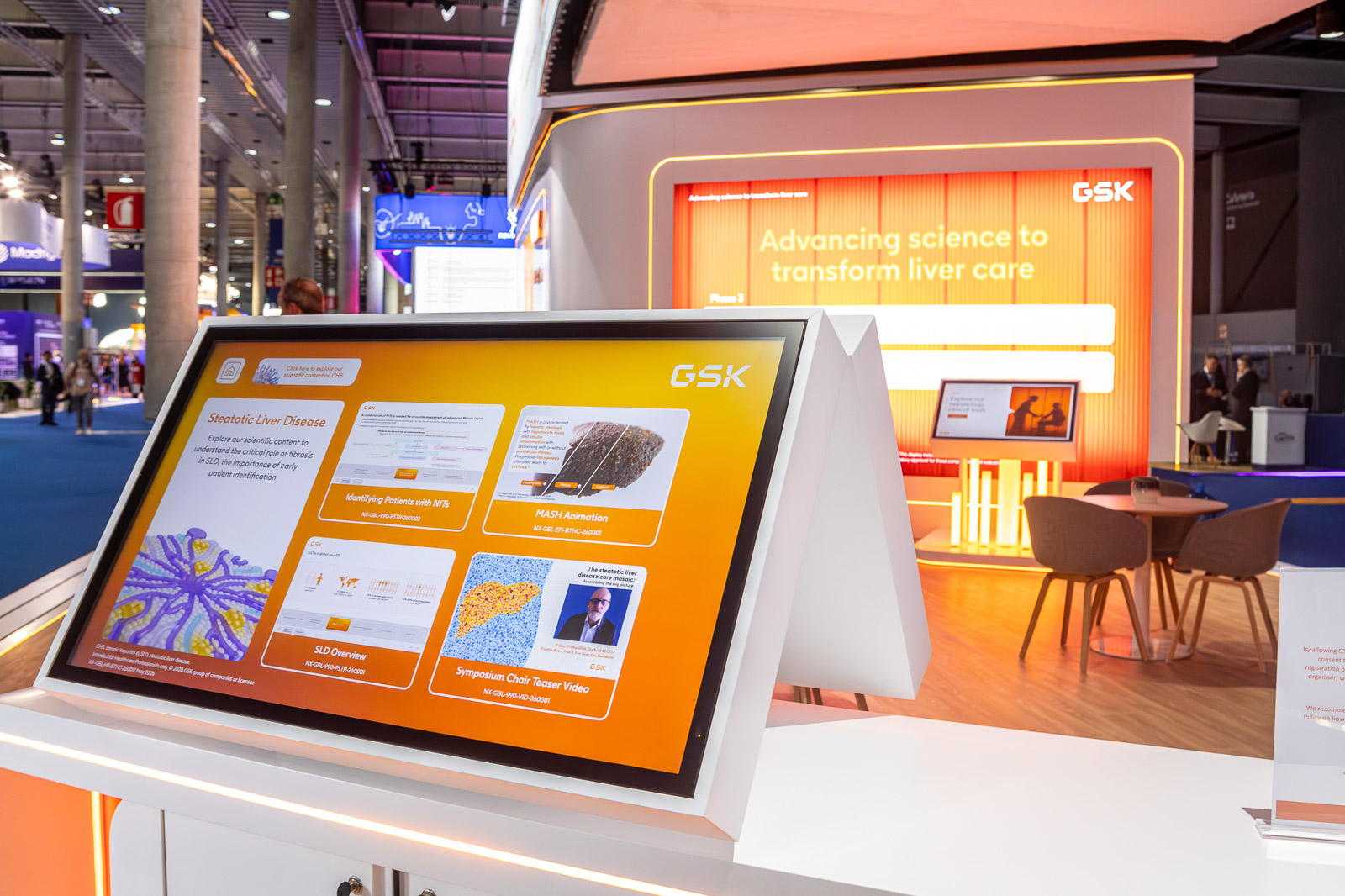 Pantalla táctil integrada en un soporte naranja del espacio expositivo de GSK.